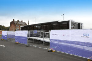 The clinical trials unit surrounded by a fence covered in white and purple banners with the trial logos