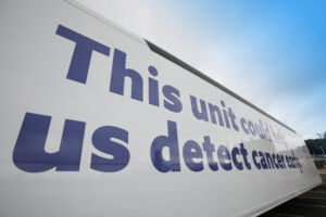 An external side of the trials unit, which is white with purple text which reads 'This unit could help us to detect cancer early'