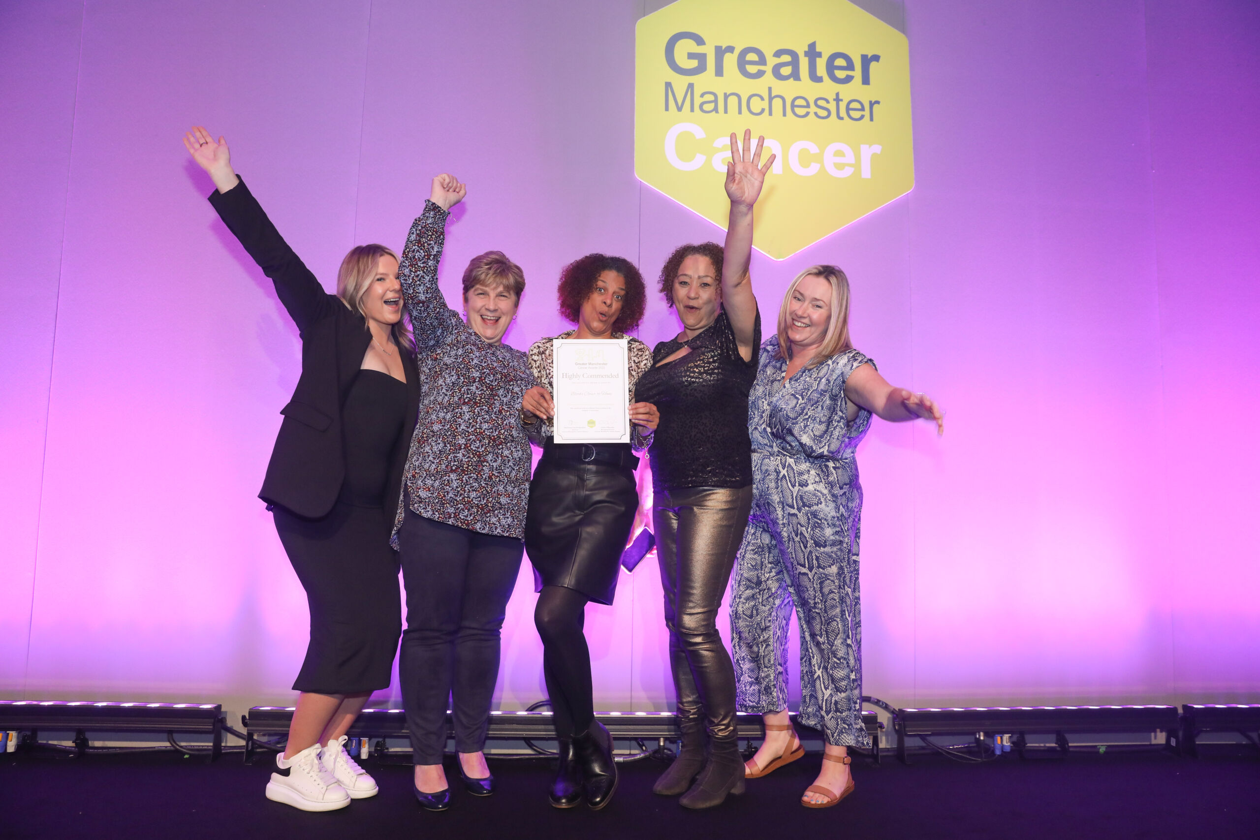 5 women pose with an awards certifucate on stage with their arms in the air
