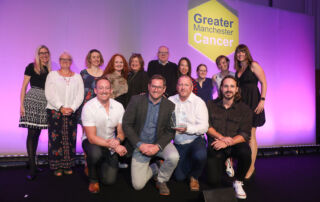 A group of men and women stand and crouch on stage as they celebrate at GM Cancer Awards
