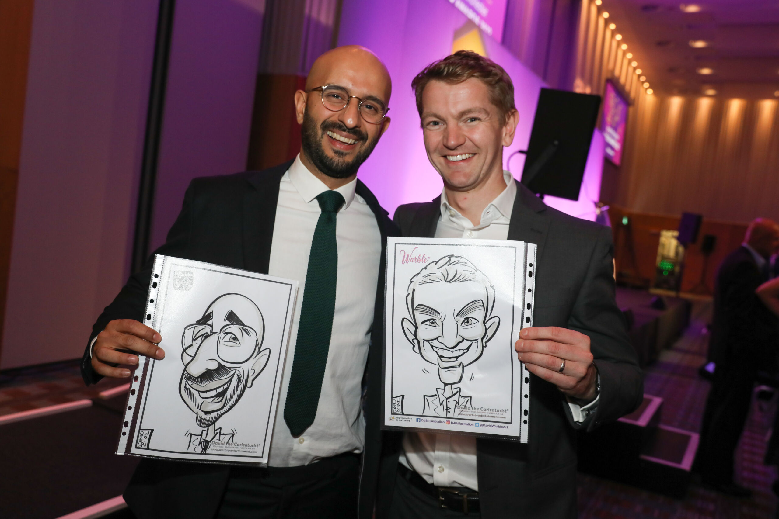 Two men in dark suits smile and hold caricatures of themselves
