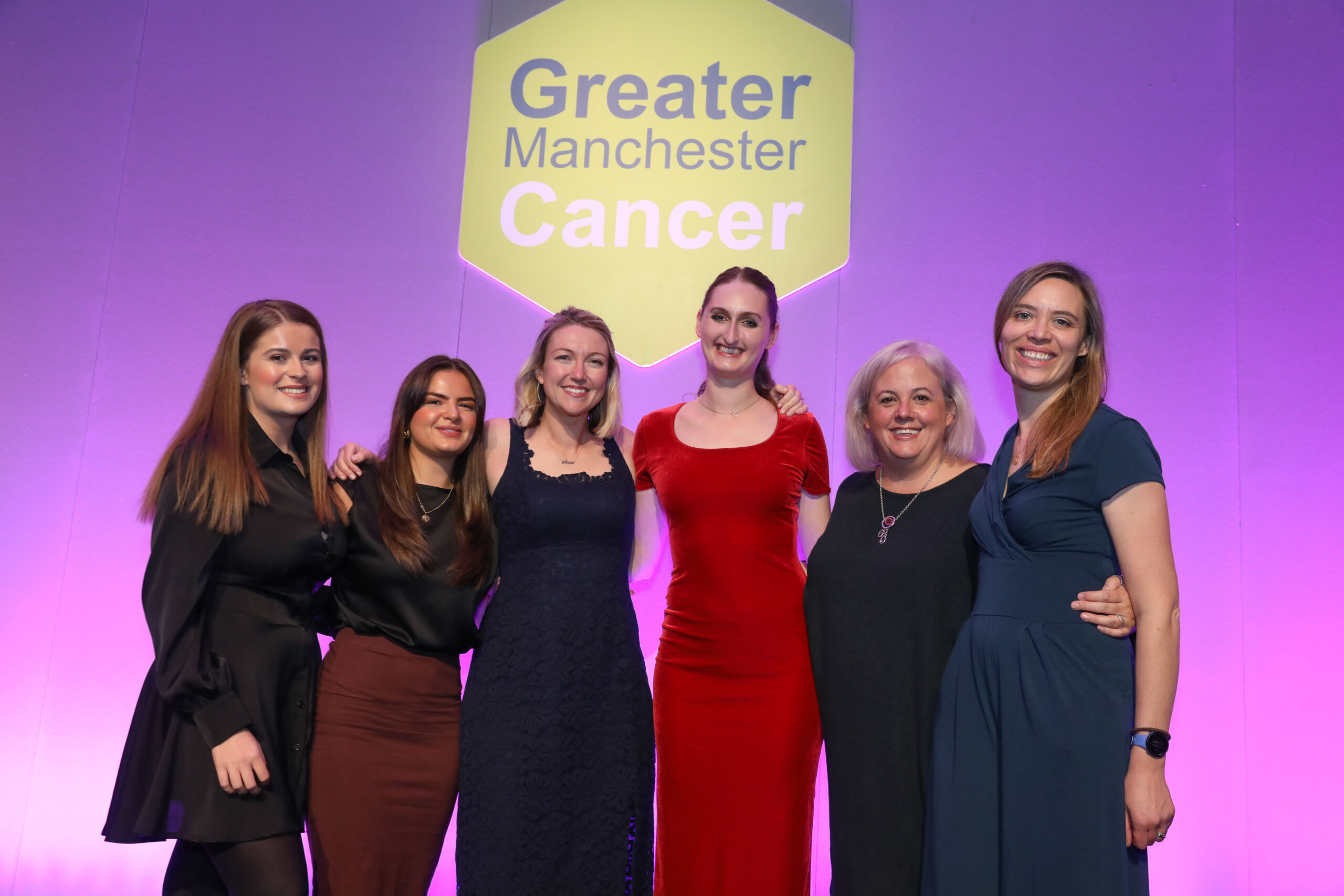 6 women with their arms around each oter on stage at the GM Cancer Awards