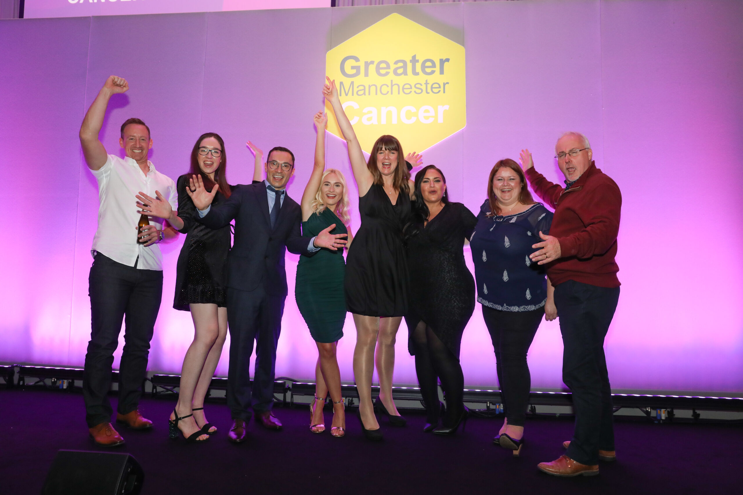 A group of 8 people on stage cheering at the Greater Manchester Cancer Awards