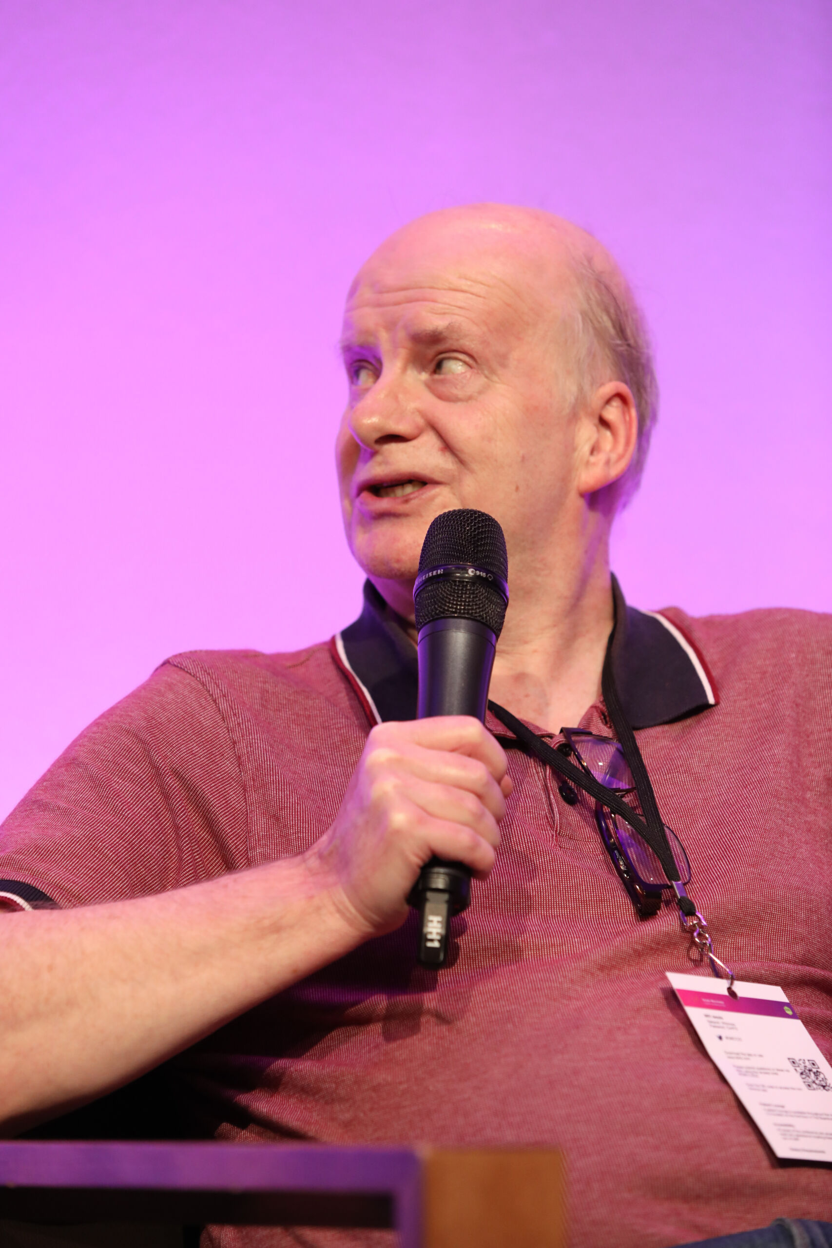 A white man in a red shirt sitting down holding a microphone