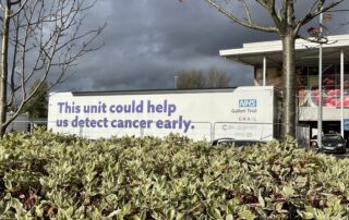 The NHS Galleri unit parked behind a green hedge in Salford