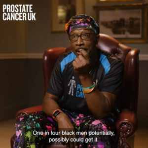 Mr Motivator sitting on a red armchair wearing a Prostate Cancer UK blue T-shirt