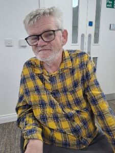 A man with grey hair and glasses in a yellow and black checked shirt
