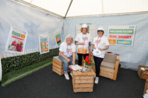 Three women in white T-shirts inside the Greater Manchester Cancer Alliance marquee at Tatton Flower Show