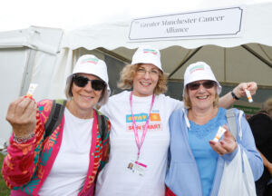 Three women wearing sun hats stand in front of a marquee