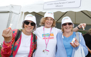 Three women wearing sun hats stand in front of a marquee