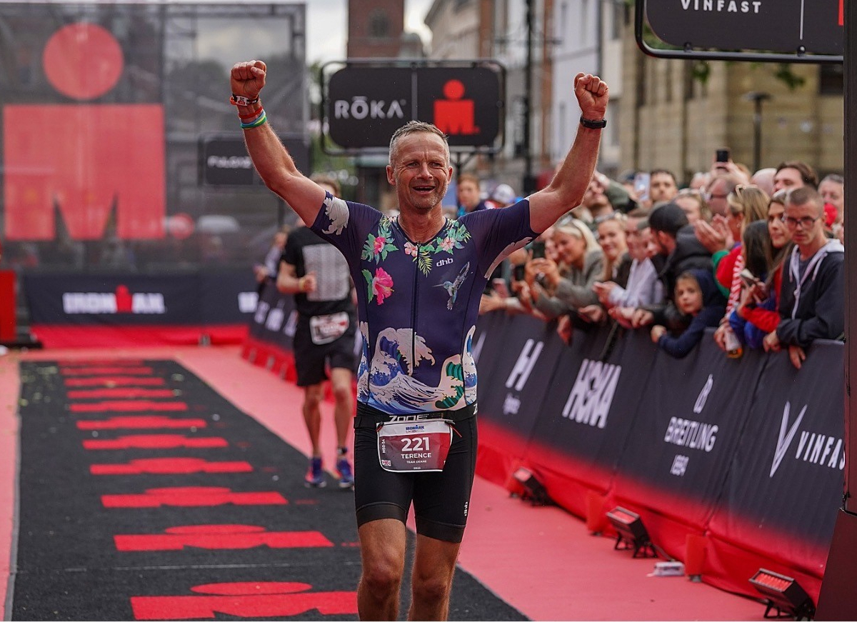 Tex at the finish line of Bolton Ironman with arms raised in celebration