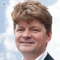 A headshot of Roger Prudham a white man standing outside with a cloudy sky behind him