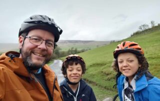 A selfie of David Jones-Stanley with his two children smiling wearing bike helmets.