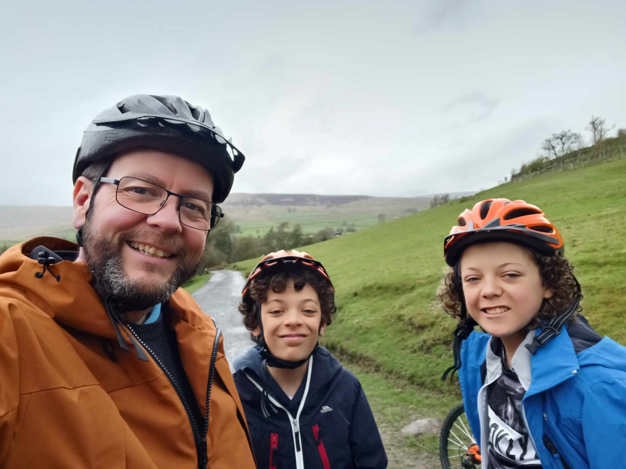 A selfie of David Jones-Stanley with his two children smiling wearing bike helmets.