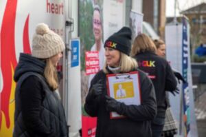 Heartburn pic for socials 1 A female team members from Heartburn Cancer UK wearing a black hat and with blonde hair talks to a a member of the public in front of a white mobile roadshow unit with orange and white stripes on the side