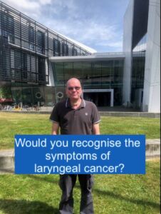 Person standing in front of a modern building with a sign asking if you would recognize the symptoms of laryngeal cancer.