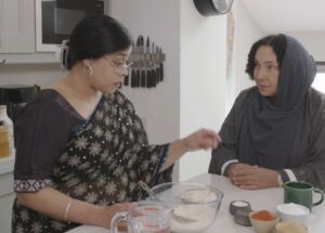 Two Asian women talk at a kitchen island while preparing food