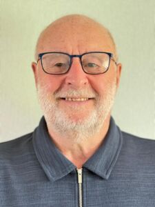 Picture of Ken Roberts wearing a blue zip up collared jumper and glasses.