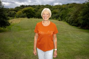 Older lady standing on a hill with an orange t-shirt with an eye and a hand on it.
