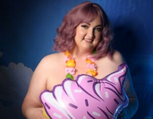 Smiling person with a lei around their neck holding a blown up ice cream cone.