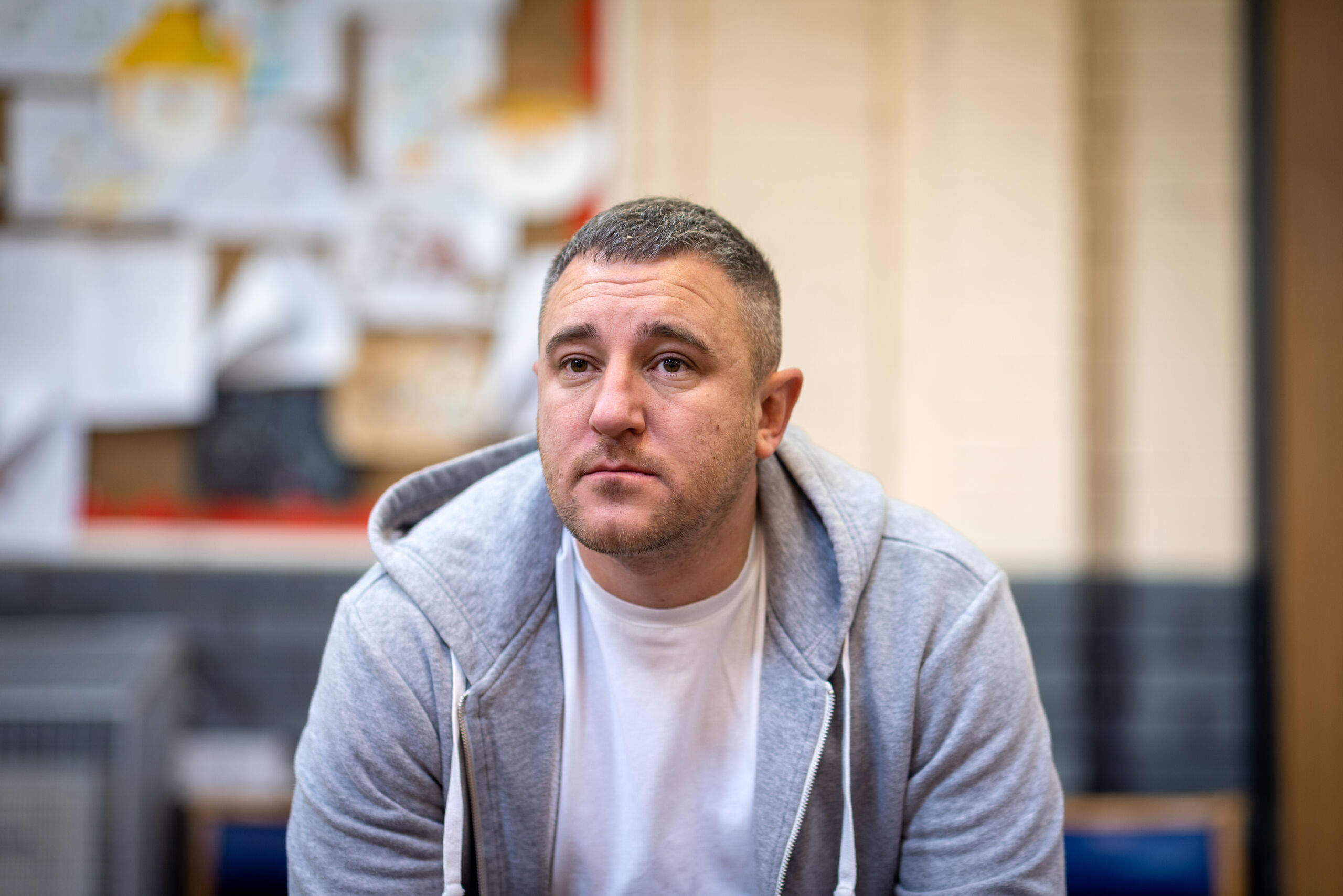 A middle-aged white man with grey hair sits down wearing a grey hoodie