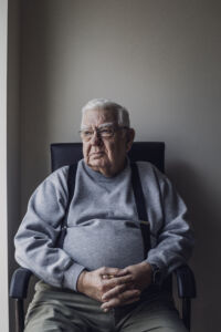Senior man sitting alone at home, his fingers are clasped together. Serious expression