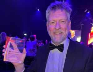 Dr Rhidian Bramley holding a transparent trophy at an awards ceremony
