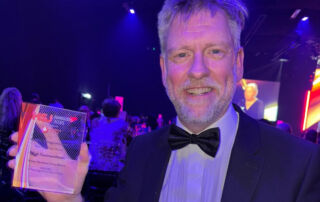 Dr Rhidian Bramley holding a transparent trophy at an awards ceremony