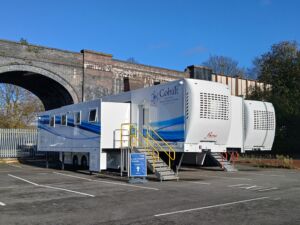 Lung Cancer Screening at Stagecoach park and ride Hazel Grove Two white trucks housing a mobile lung cancer screening service in front of an arch in a car park