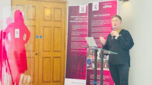 The-late-Jo-Taylor-(a white woman with short hair wearing black - stands on-stage-at-the-Greater-Manchester-Metastatic-Breast-Cancer-Conference