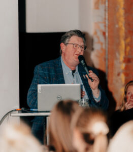 Image of a man in front of a podium in a blue suit with a microphone.