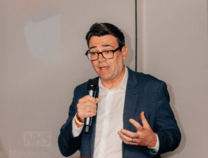 Andy Burnham at the Mets launch Cropped Andy Burnham, the Mayor of Greater Manchester with a microphone speaking at a conference.