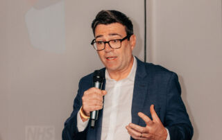 Andy Burnham, the Mayor of Greater Manchester with a microphone speaking at a conference.
