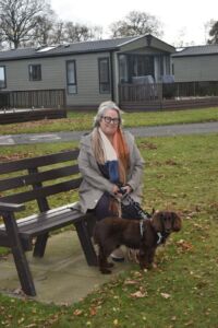 Gillian Glynn a white woman in her 60s stands by a bench with a dog