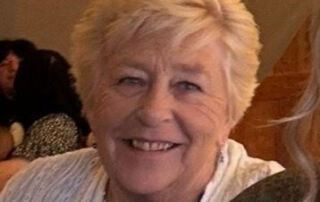 A head and shoulders image of Linda Cotterell, a white woman with short hair in her 70s smiles at the camera