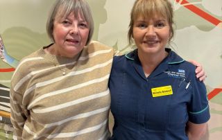 Catherine, a white woman with short grey hair in a stripey jumper stands next to Michelle a white woman with a fringe and her hair tied back wearing a nursing uniform