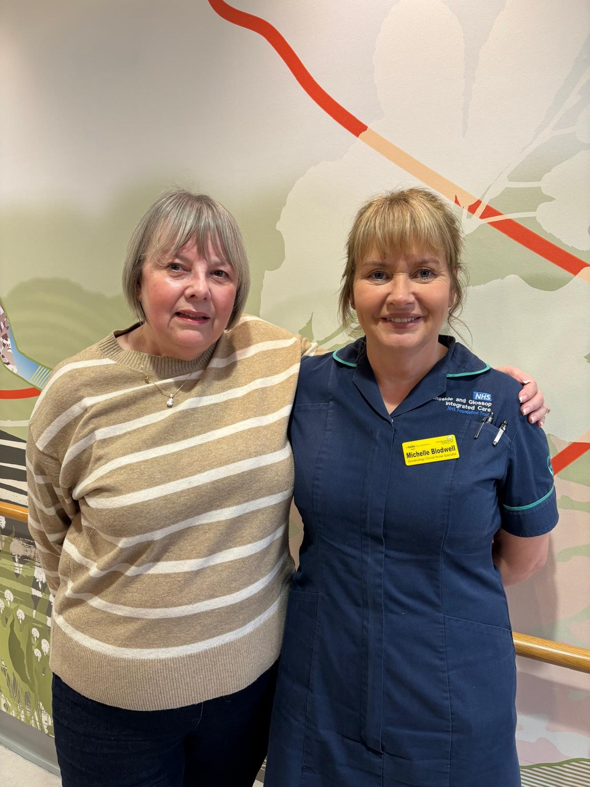 Catherine, a white woman with short grey hair in a stripey jumper stands next to Michelle a white woman with a fringe and her hair tied back wearing a nursing uniform