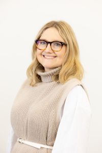 A head and shoulders image of Dr Helena O'Flynn a white woman with blonde shoulder length hair and glasses smiles at the camera. 