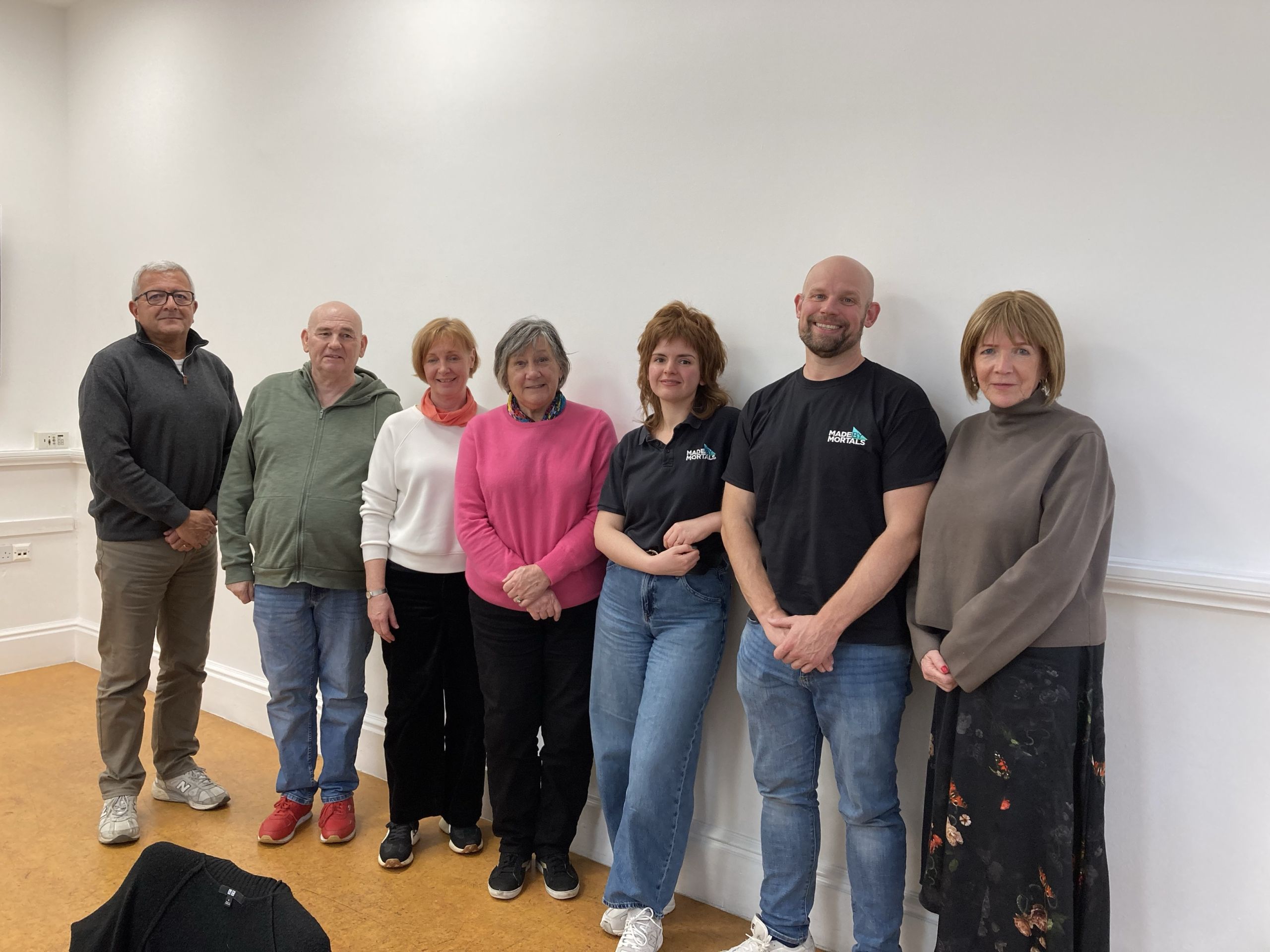 A group of seven men and woman who are patient carers standing against a white wall in casual clothes with two members of staff from Made by Mortals