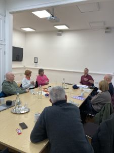 A group of male and female carer representatives sit around a large table discussion their experiences