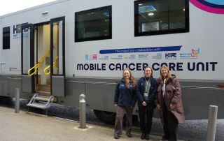 Three NHS staff stand in front of the new mobile cancer care unit for Greater Manchester