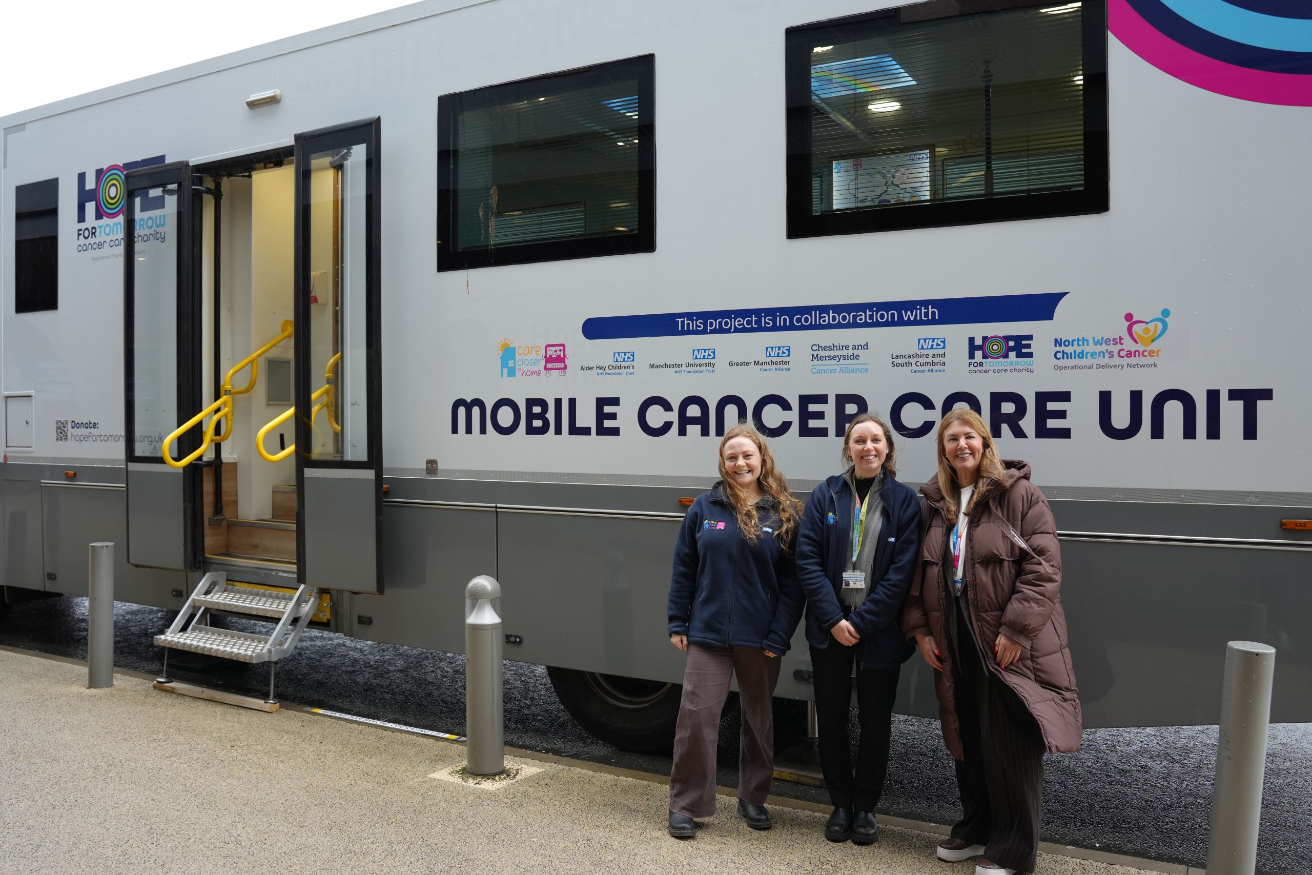 Three NHS staff stand in front of the new mobile cancer care unit for Greater Manchester