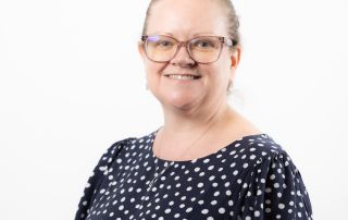 Louise Brown, Clinical Lead for Lung Cancer at Greater Manchester Cancer Alliance smiling and wearing glasses and a patterned top.