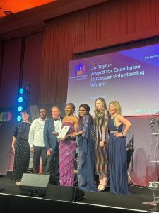 Maria Lawal wearing a long pink dress on stage with John Thomson and a group of people to collect her award