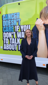 Runner Paula Radcliffe in front of the green This Van Can Cancer Awareness Roadshow with the words "Cancer Doesn't care if you don't want to talk about it" 