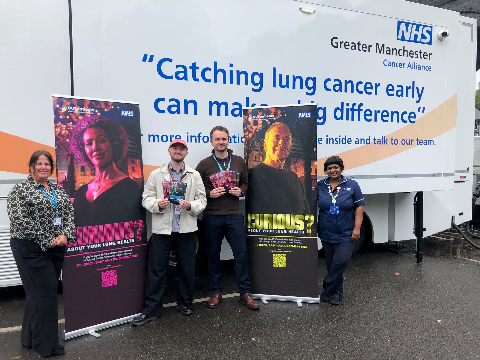 Four people including a nurse stand outside the NHS Lung Cancer Screening mobile clinic with two new pull up banners aimed at the LBGTQI+ community asking people to Get Curious About Their Lung Health