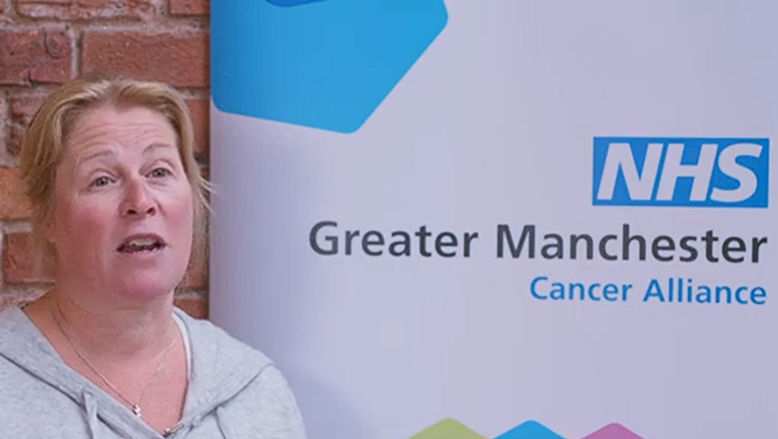 Susi - a woman with blonde hair in a pony tail - talks to the camera in front of a Greater Manchester Cancer Alliance back drop