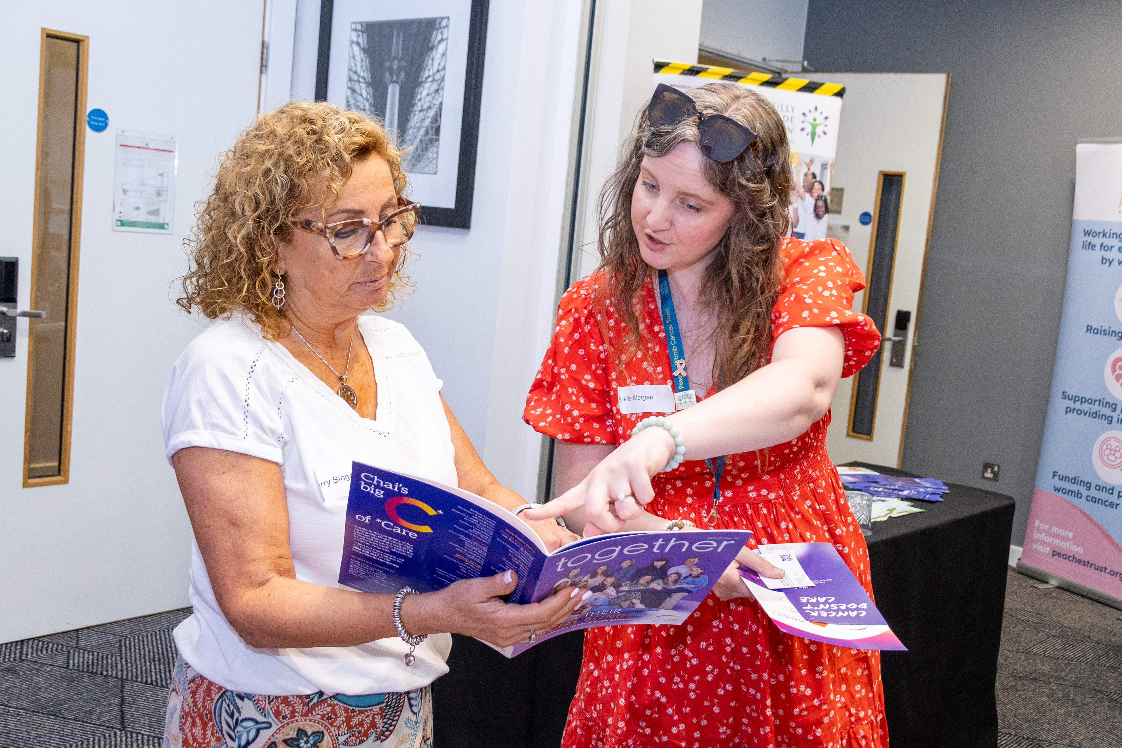 16 Joelle from Peaches Womb Cancer Charity speaking with a delegate at the conference holding a booklet. Joelle is pointing to information in the booklet and talking.