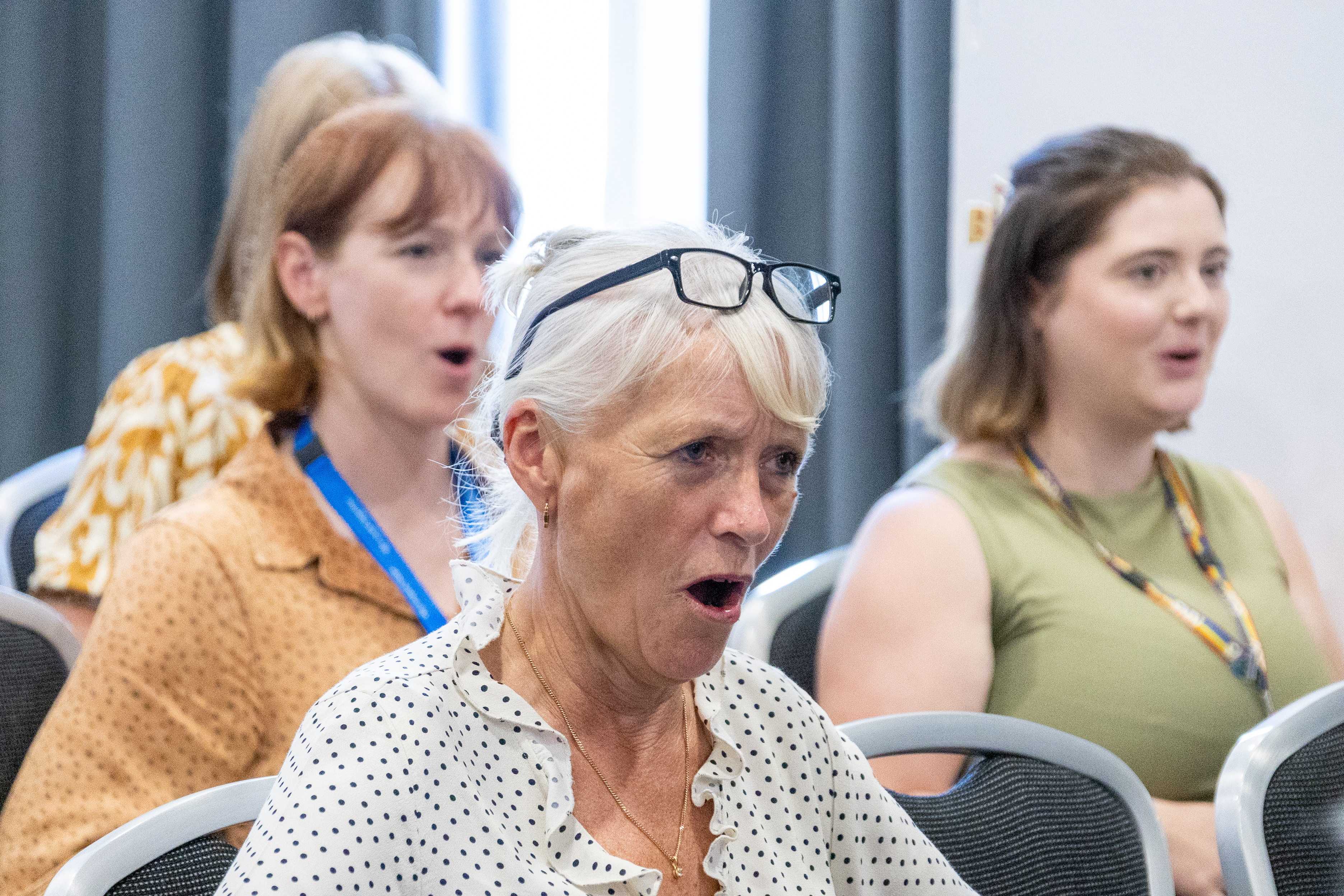 19 A group of attendees taking part in a guided laughter therapy session with focus on a woman in a polka dot top