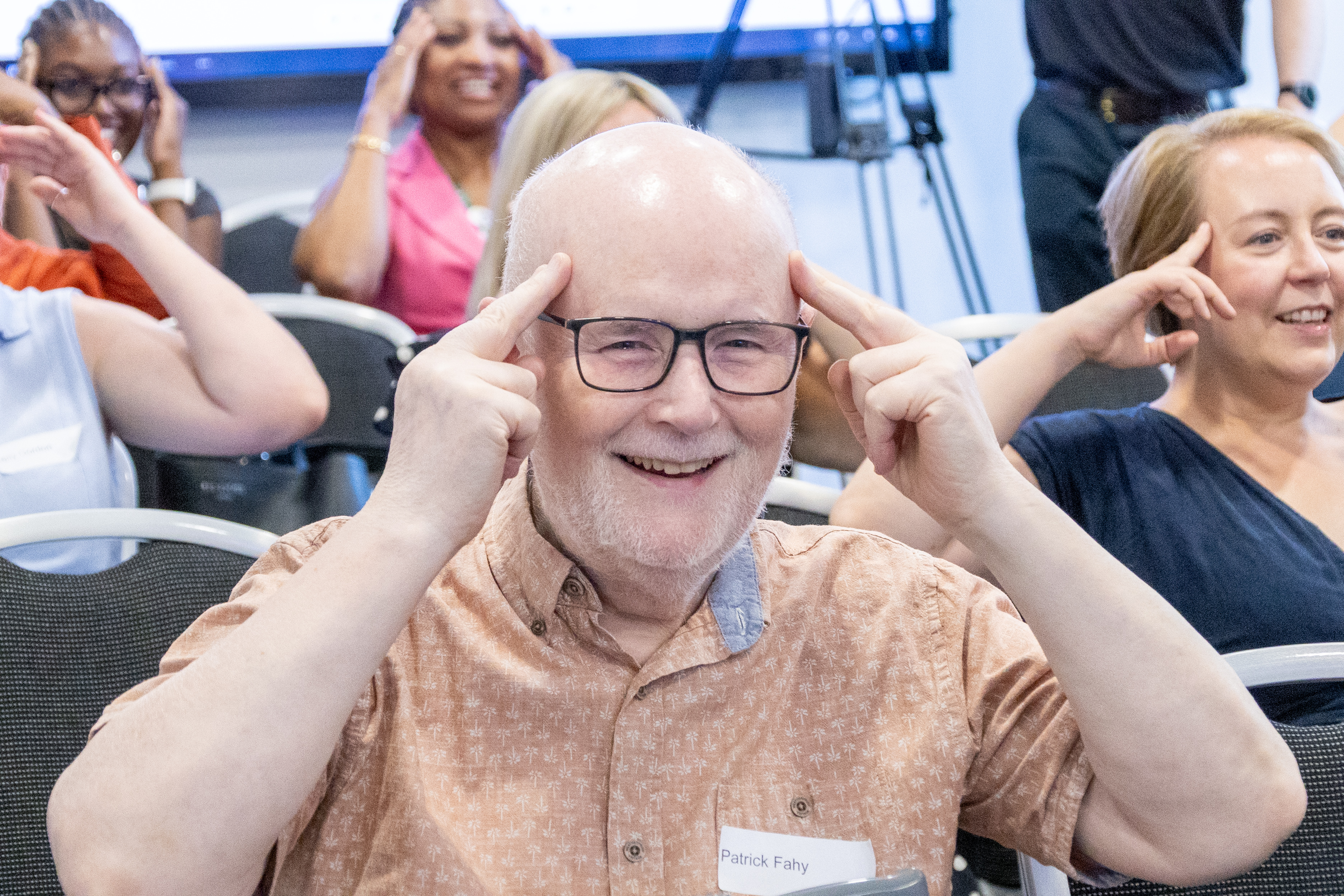20 Close up of Patrick Fahy a patient representative sat in the audience participating in chair yoga with his hands on his temple smiling